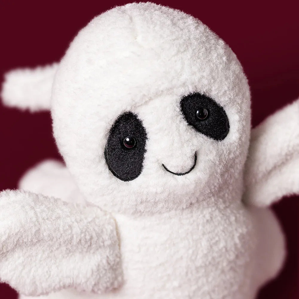 A close-up of a white plush ghost toy with black embroidered eyes, a curved smile, and small wings, set against a dark burgundy background.