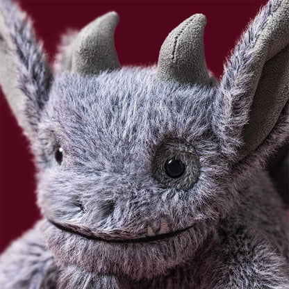A close-up of a gargoyle toy with pointed ears, dark eyes, and a stitched smile against a dark red background.