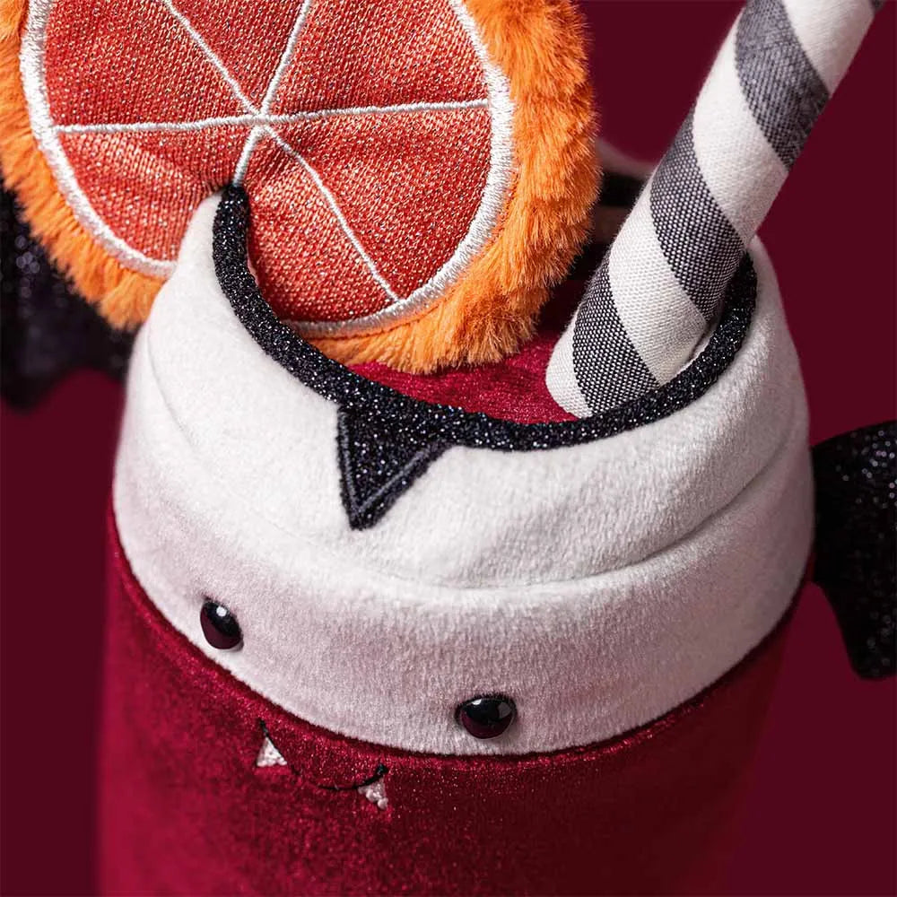 A close-up of a plush Halloween drink cup decoration, featuring a red velvet-like body, white plush whipped cream top, black glitter trim, a striped gray-and-white straw, and an orange slice accent on a dark red background.