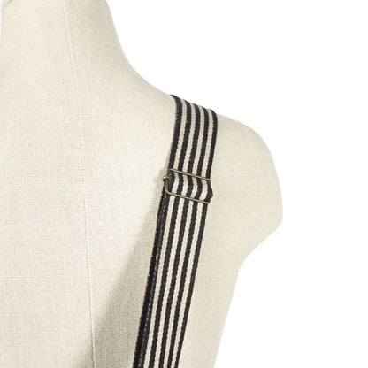 Black and white striped canvas shoulder strap with a brass buckle, shown on a cream linen mannequin torso against a white background.