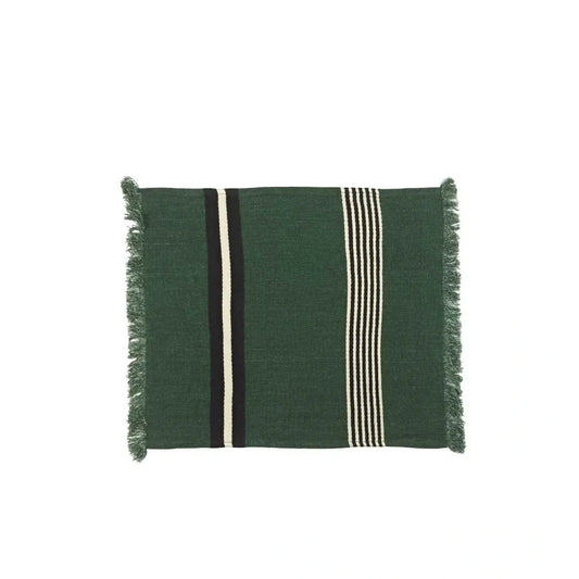 A square dark green woven linen placemat with fringed edges, featuring vertical stripes in black, cream, and white.