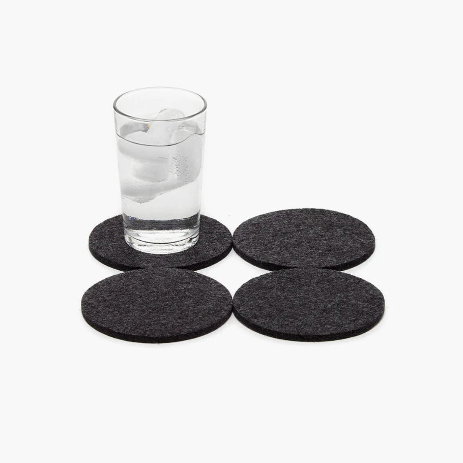 Four dark gray coasters on a white background with a glass of water.