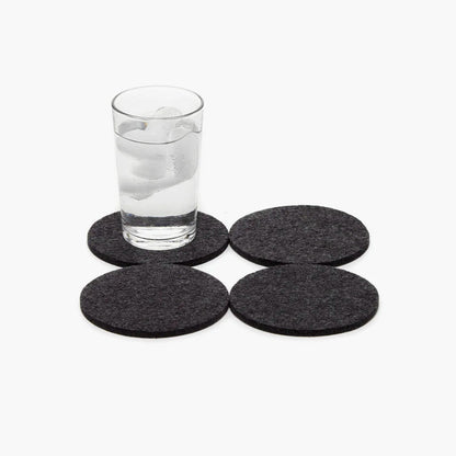 Four dark gray coasters on a white background with a glass of water.