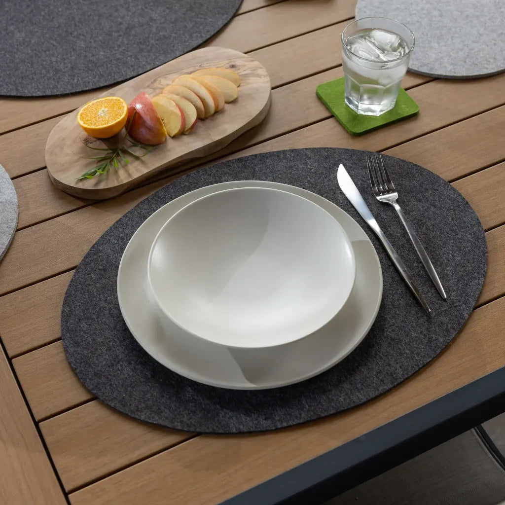 Dining setup with a white bowl, knife, fork, and glass on a wooden table with charcoal oval placemats.