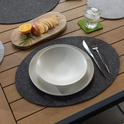Dining setup with a white bowl, knife, fork, and glass on a wooden table with charcoal oval placemats.
