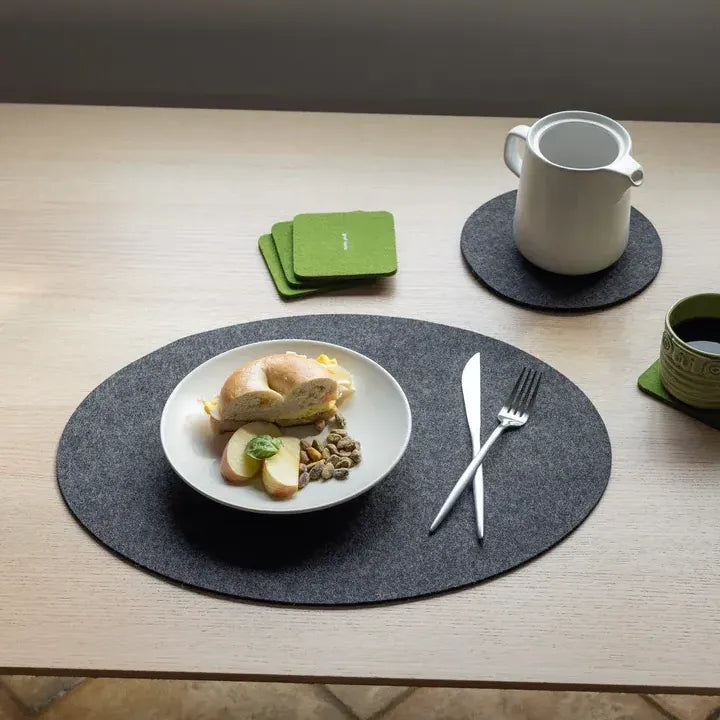 Table setting with a plate of food, cutlery, and coasters on a wooden table.