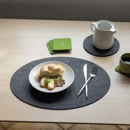 Table setting with a plate of food, cutlery, and coasters on a wooden table.