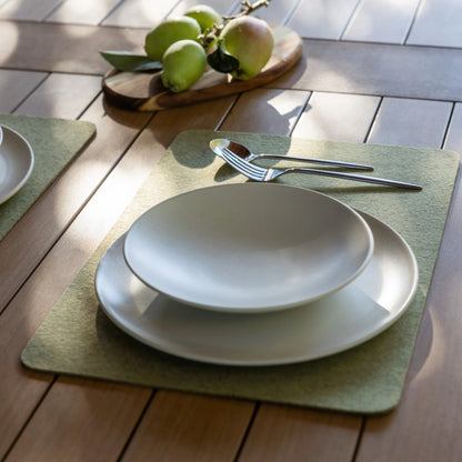White ceramic plates on green placemats with cutlery on a wooden table.