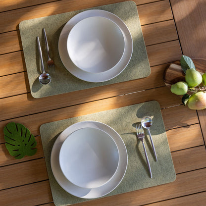 Two white bowls on green placemats with cutlery on a wooden surface.