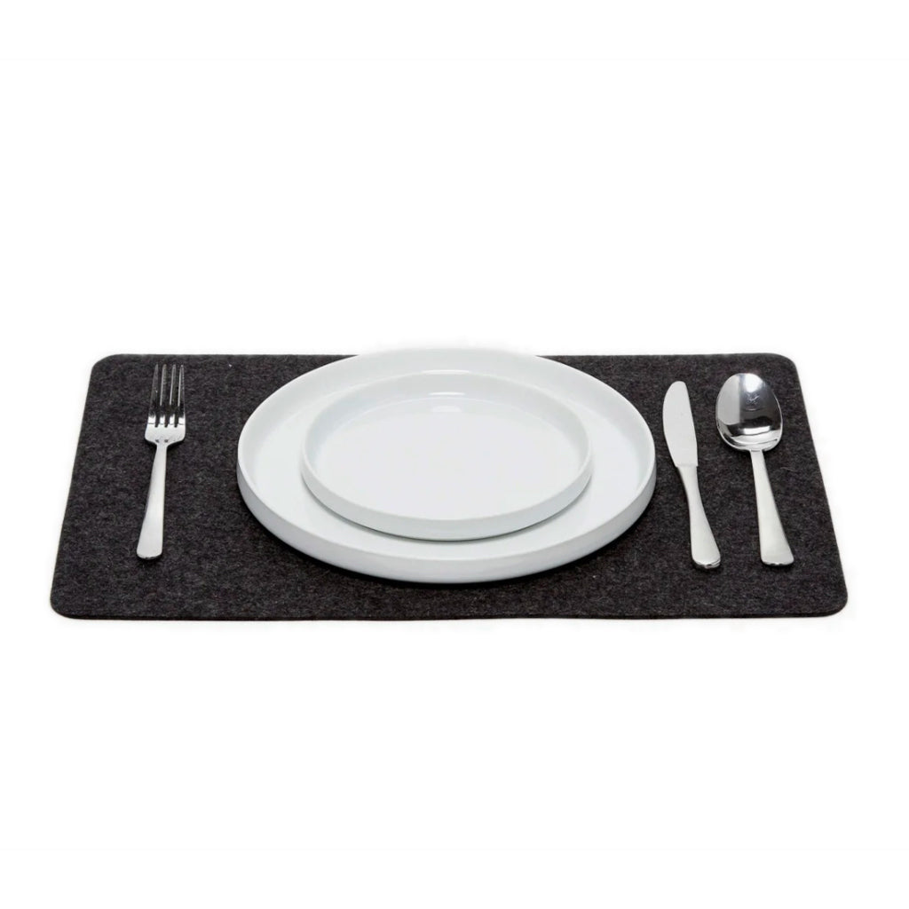 A charcoal-coloured Merino wool rectangle placemat on a white plate with silverware on top, placed on a white background.