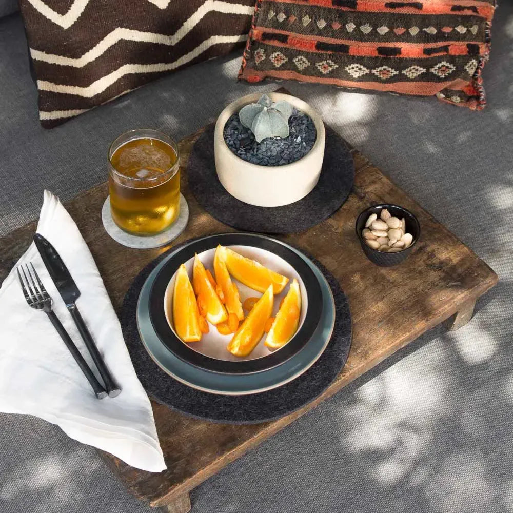 Graf Lantz Merino Wool Round Trivet in Charcoal  on a wooden tray holding a plate