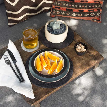 Graf Lantz Merino Wool Round Trivet in Charcoal  on a wooden tray holding a plate