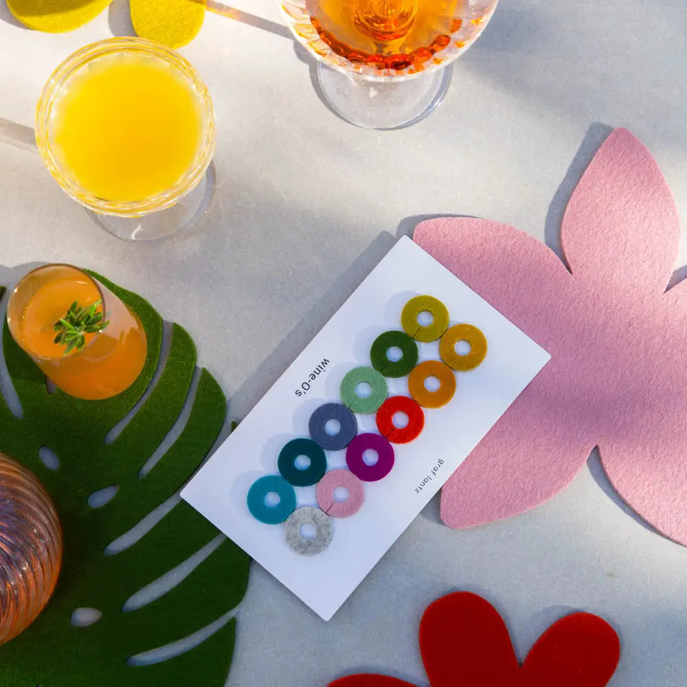 Colourful wine markers on a card with drinks and decorative coasters on a table