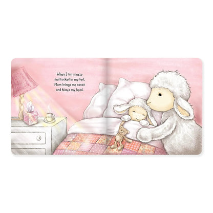 A square product shot of a printed illustration or card showing a sheep hugging a baby sheep in bed, with a bedside table and lamp on the left and a short text quote. The artwork is centered on a plain white background.