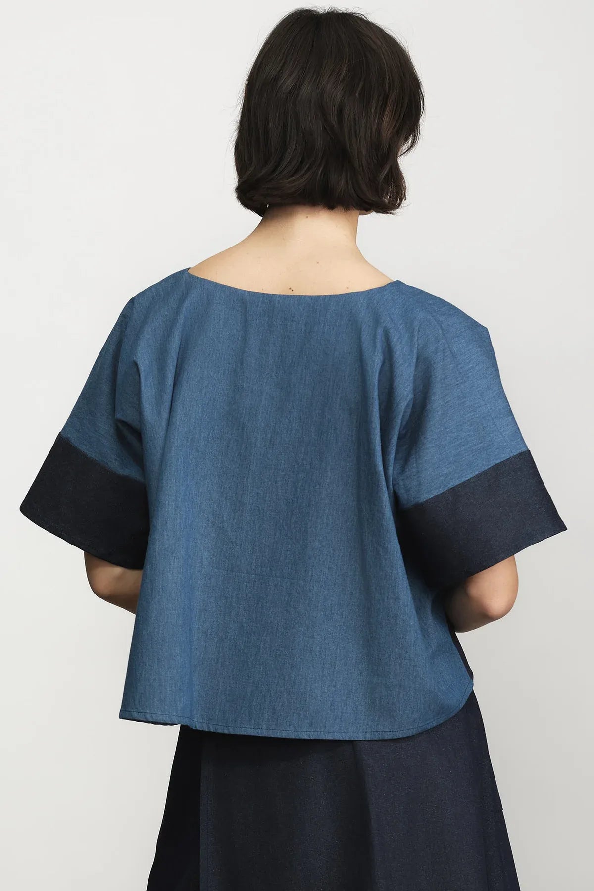 A person shown from the back wearing a loose blue top with contrasting dark navy sleeve cuffs and a dark navy skirt, photographed against a plain light background.