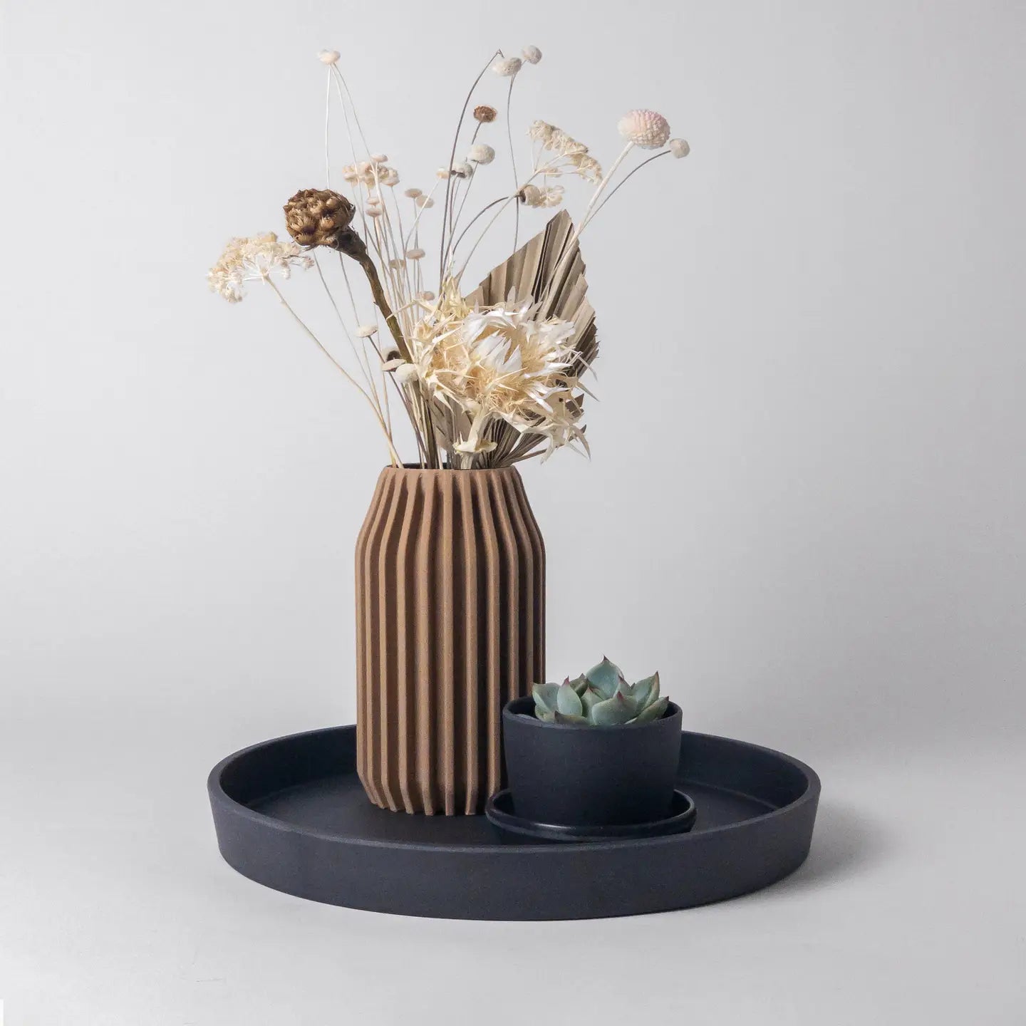 Decorative setup with a striped vase, small plant, and black tray on a light gray background
