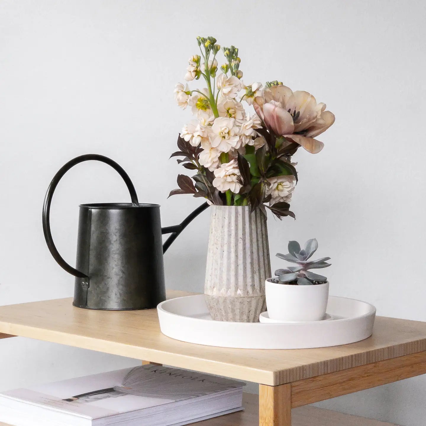 Decorative items including a black watering can, vase with flowers, and small potted plant on a wooden table.