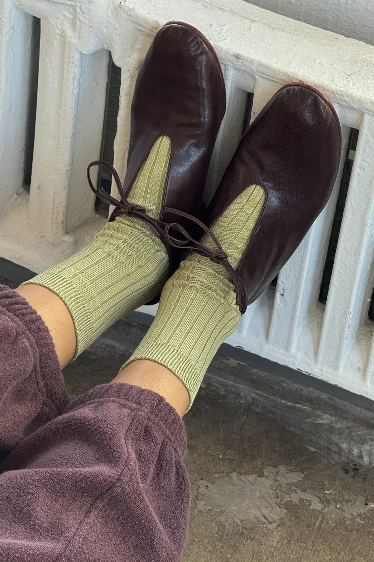 Green socks being worn, with brown leather shoes with a white railing in the background.