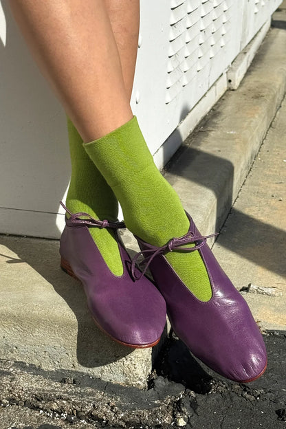 Purple shoes and green socks worn by a person on a concrete step.