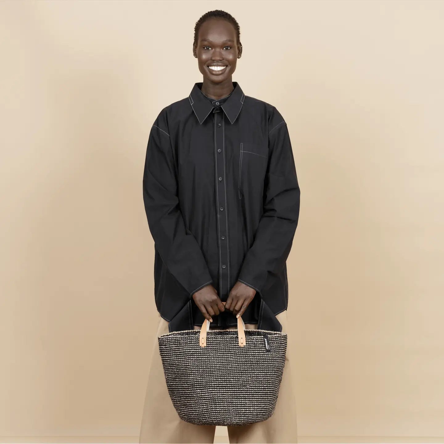 Person holding a woven bag against a beige background