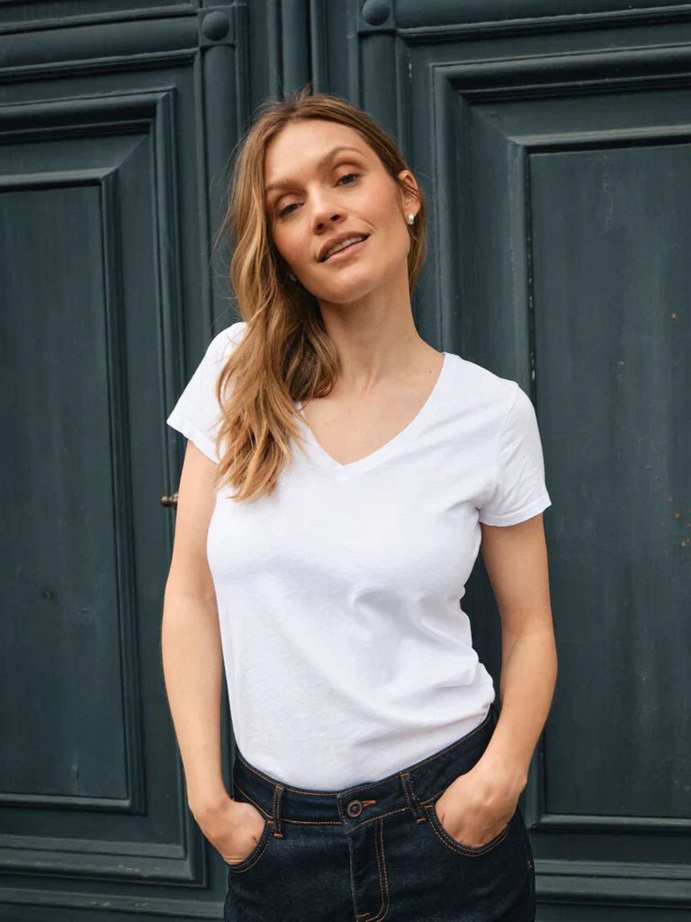 Woman wearing a white t-shirt and dark jeans standing in front of a dark green door.