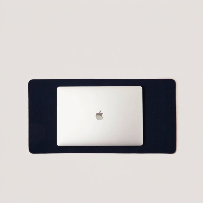 A medium-sized, navy blue desk pad with a corner of a white laptop visible, showcasing the product's size and fit.