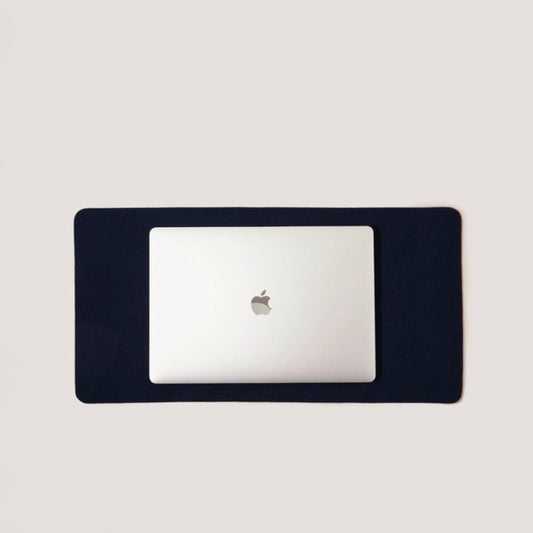 A medium-sized, navy blue desk pad with a corner of a white laptop visible, showcasing the product's size and fit.
