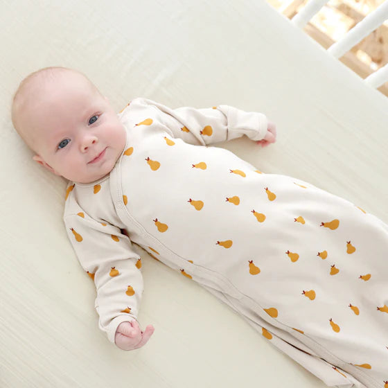 Baby lying on a crib wearing a white onesie with orange patterns