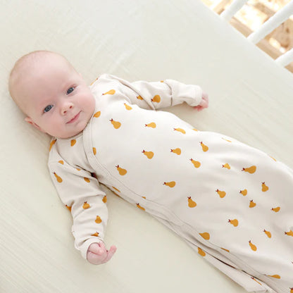 Baby lying on a crib wearing a white onesie with orange patterns