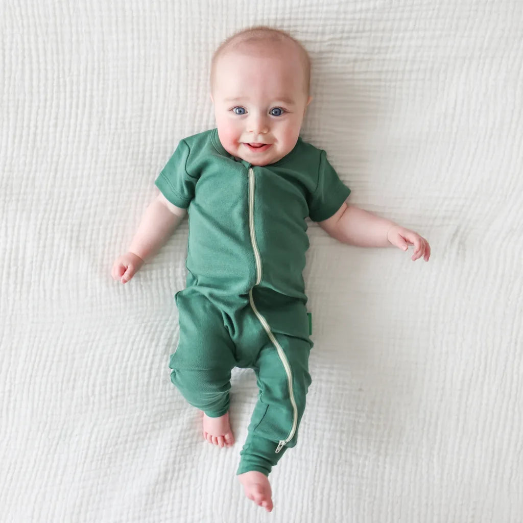 Baby wearing a green onesie with a zipper on a white blanket