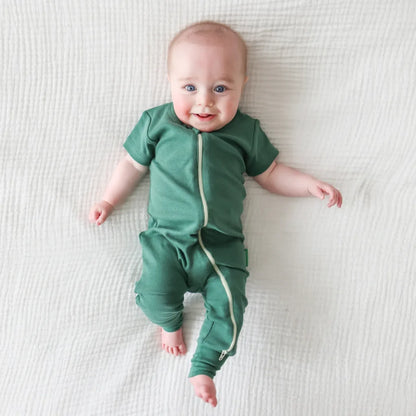 Baby wearing a green onesie with a zipper on a white blanket