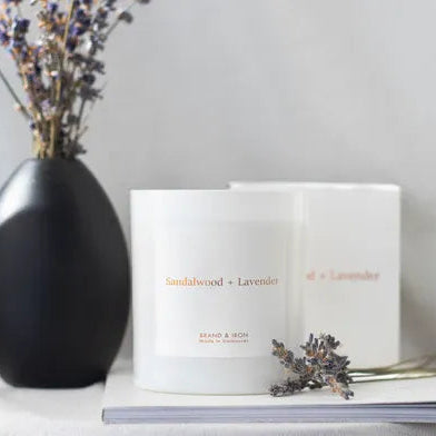Two white boxes labeled 'Sandalwood + Lavender' next to a black vase with dried flowers on a light gray surface.