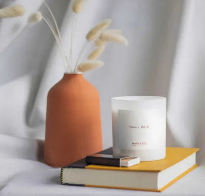 Candle, books, and vase on a light surface with a neutral background