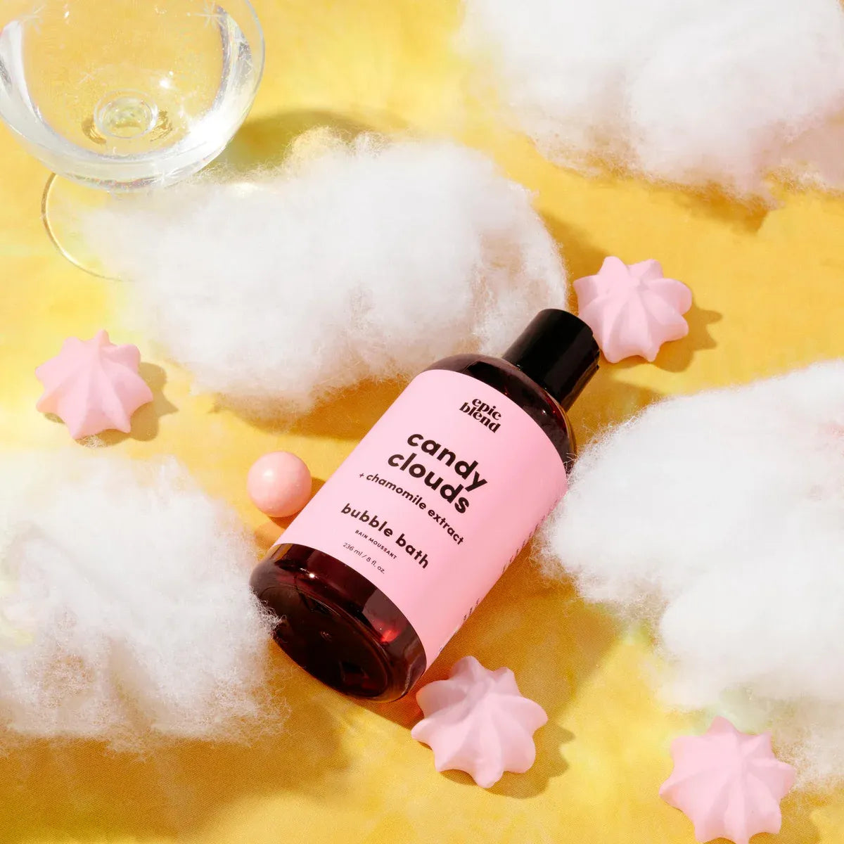 Bottle of 'candy clouds' bubble bath with cotton candy and a glass on a yellow background