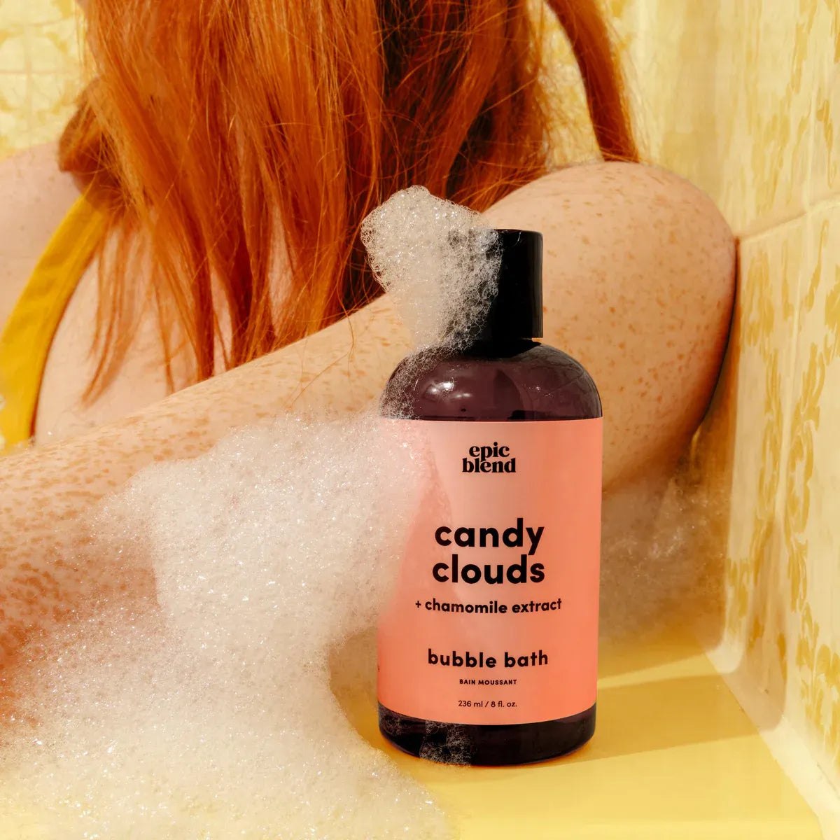 Bottle of 'Candy Clouds' bubble bath with a person in a bathtub filled with bubbles.