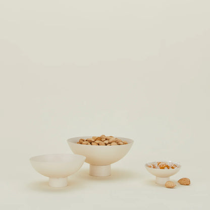 A set of three beige, powder-coated stainless steel footed bowls of various sizes, with one containing nuts displayed in the foreground.