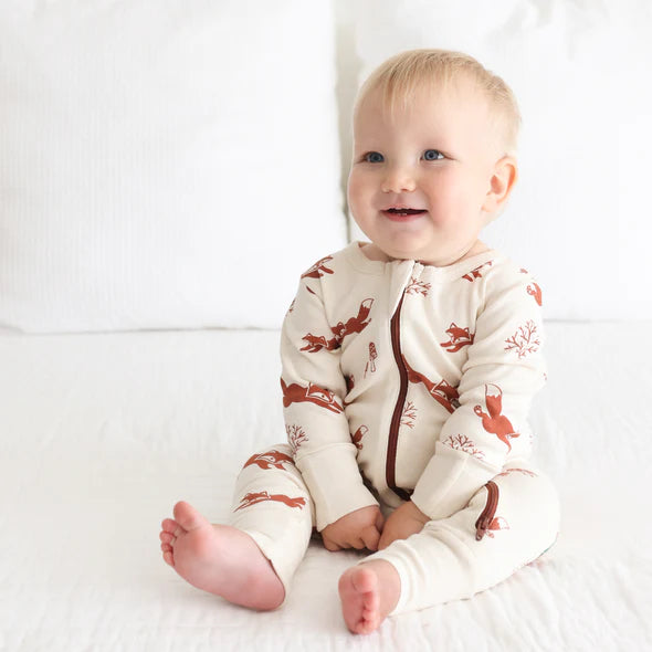 A baby wearing a beige and brown romper with a fox pattern, sitting on a flat surface.