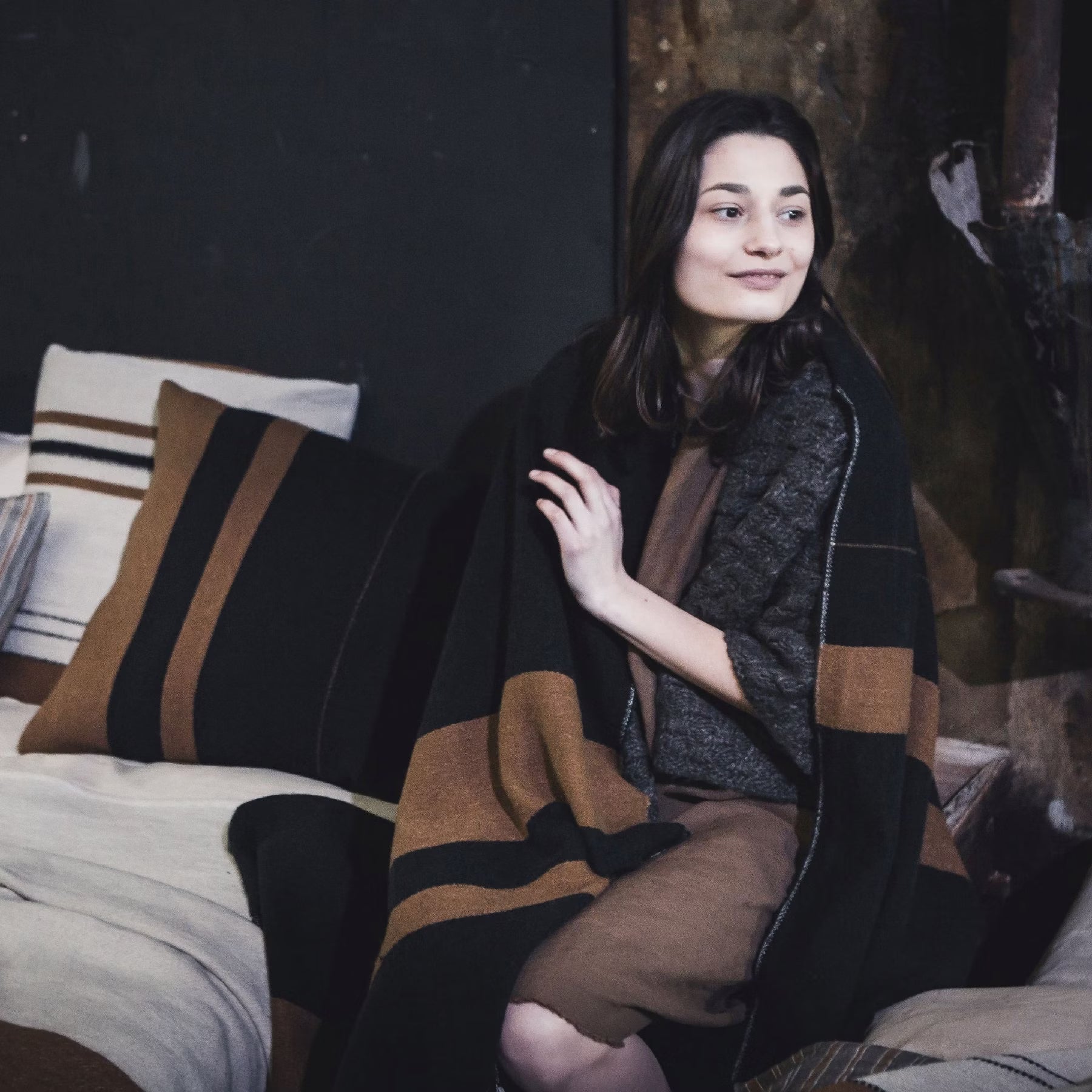 Woman sitting on a bed wrapped in Libeco Oscar Linen/Wool Throw