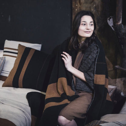 Woman sitting on a bed wrapped in Libeco Oscar Linen/Wool Throw