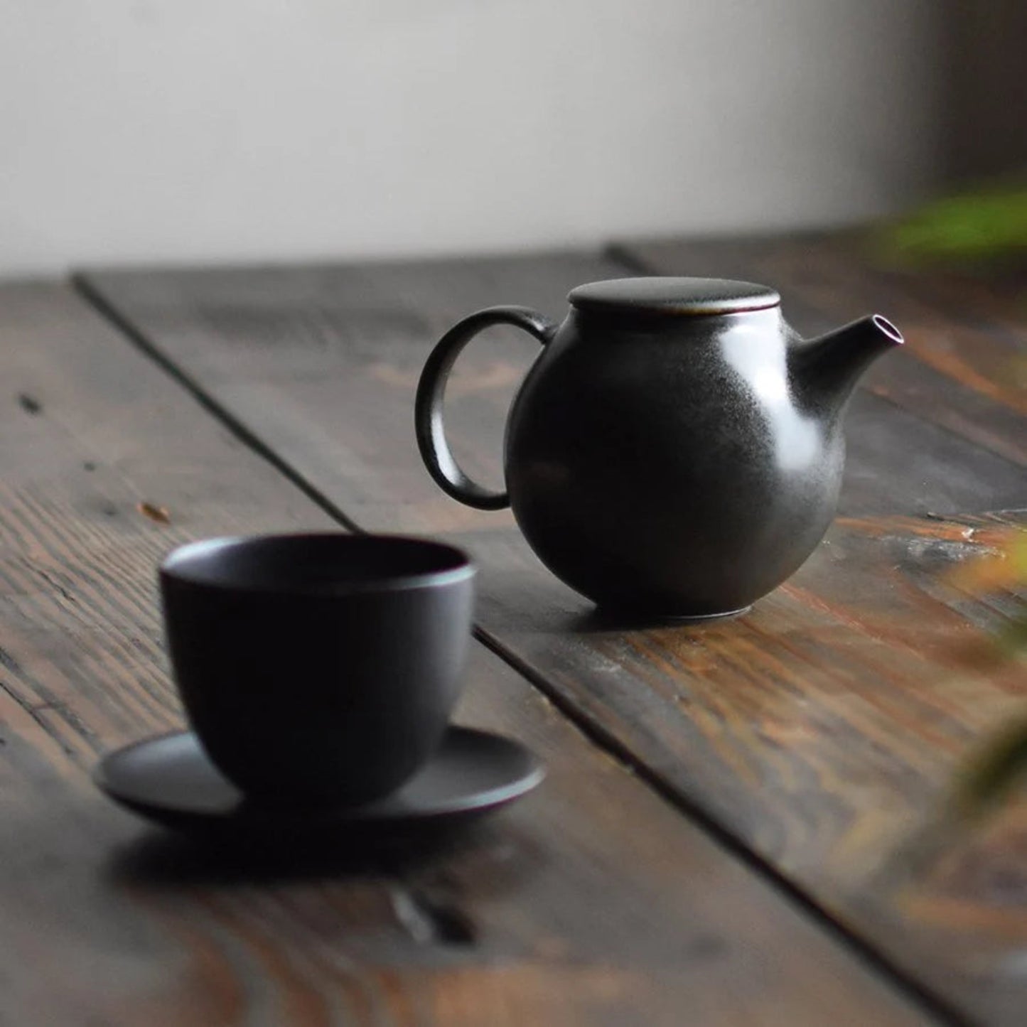KINTO PEBBLE Teapot in Black, 500ml next to tea cup and saucer