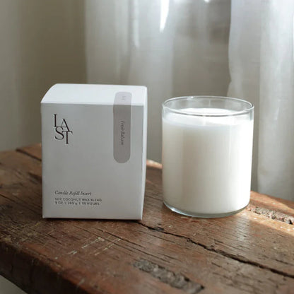 Candle refill insert packaging next to a candle on a wooden surface