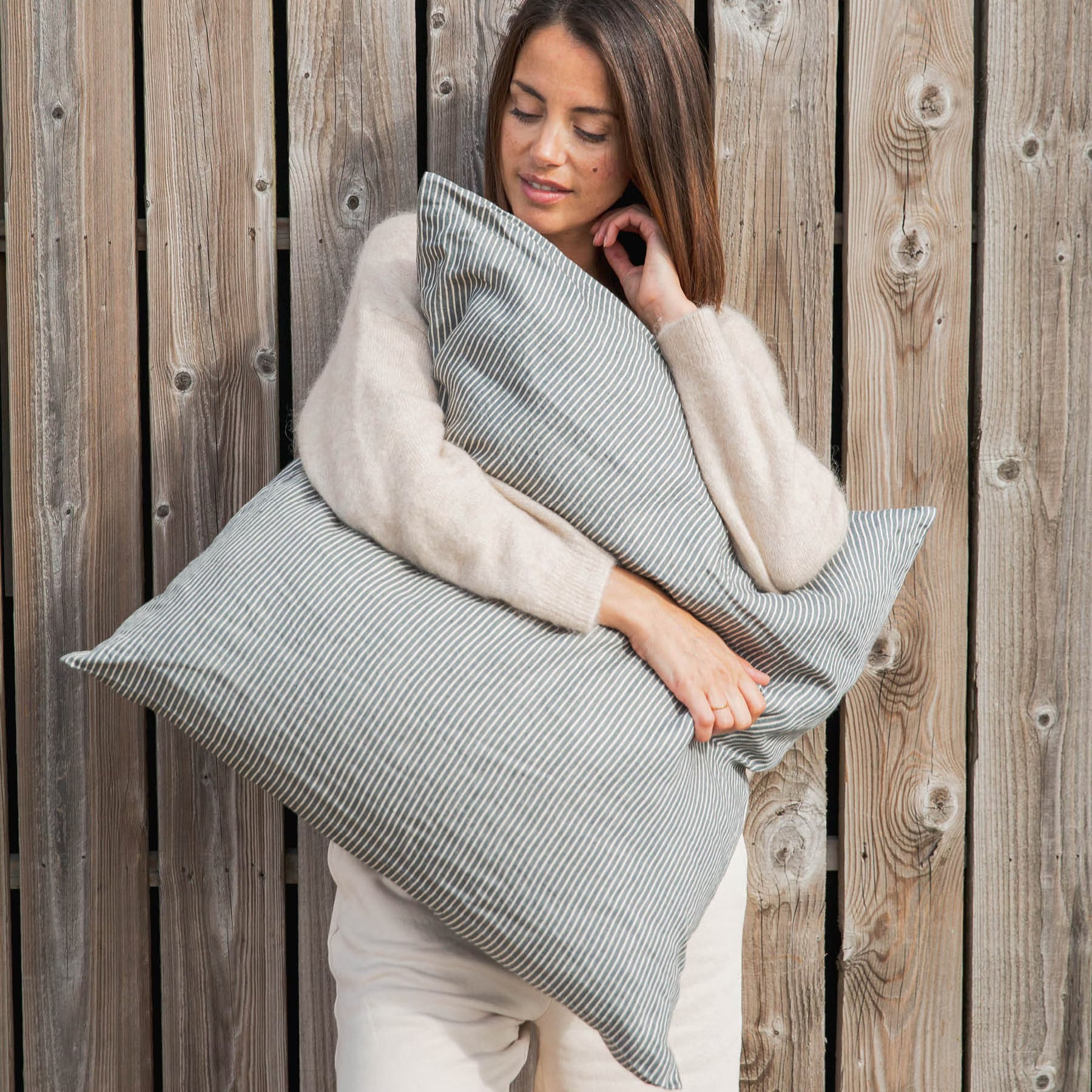Woman holding Libeco Sailors Stripe Pillow against a wooden background