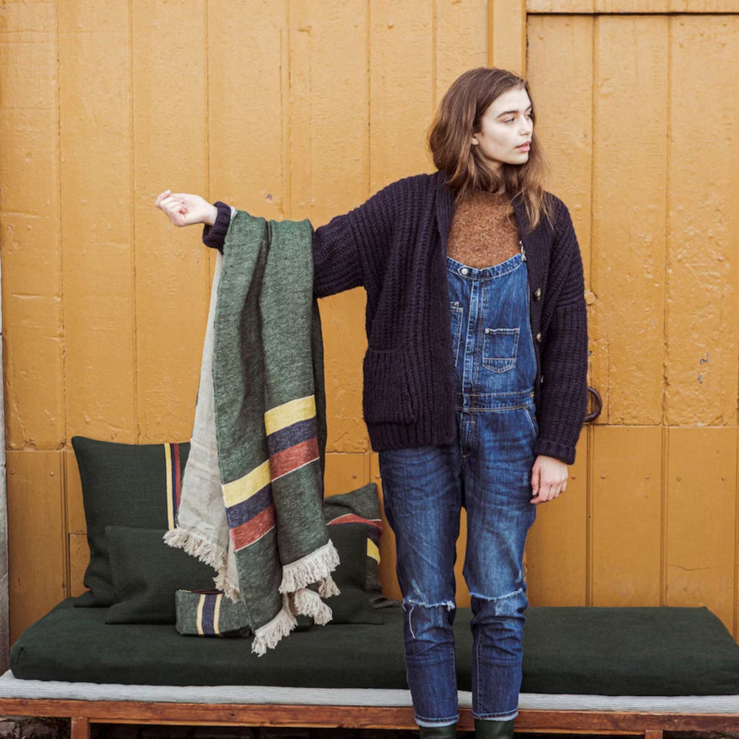 Woman holding Libeco The Belgian Towel Fouta in Spruce against a wooden wall.