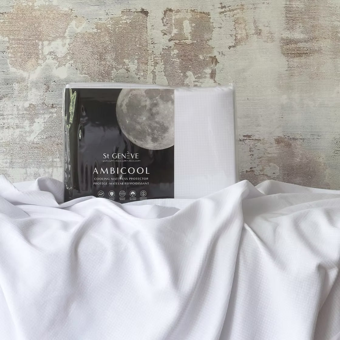 A fittedAmbiCool cooling mattress protector displayed on a bed with a moon and clouds design on the packaging.