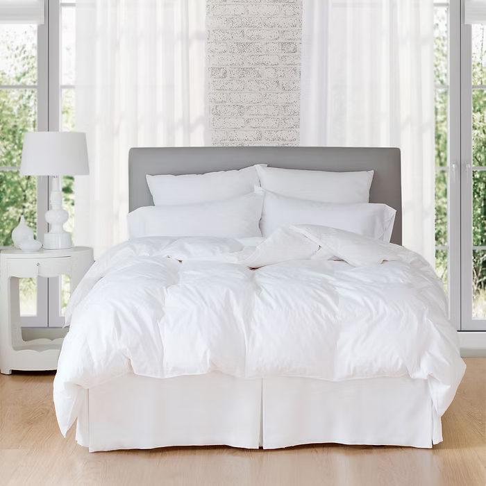White bedding set on a bed in a bright bedroom with large windows.