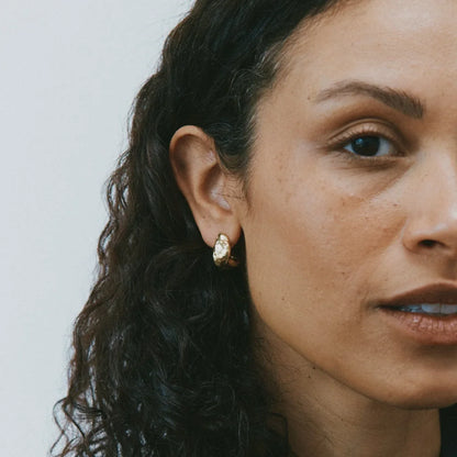 Close-up of a woman wearing a gold earring against a neutral background