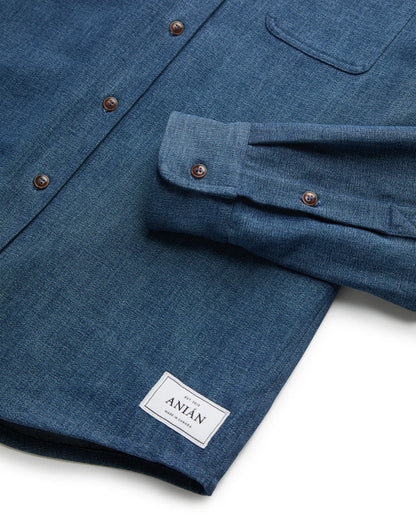 CLOSE UP OF ONE CUFF HEM OF DARK BLUE DENIM SHIRT LAID FLAT AGAINST WHITE BACKGROUND 