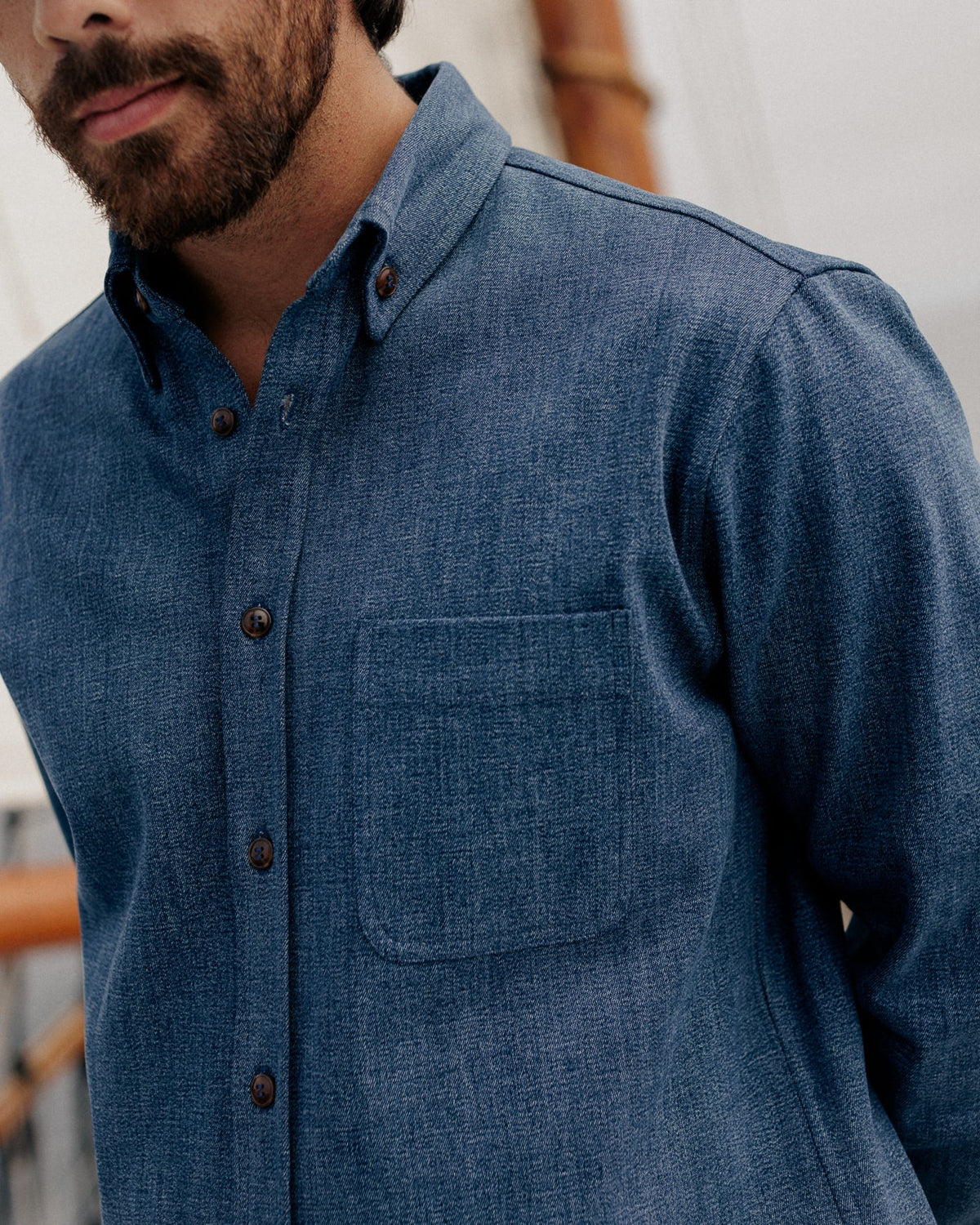 CROPPED PHOTO OF MALE MODEL WEARING DARK BLUE DENIM SHIRT, DETAIL SHOT OF COLLAR AND FRONT POCKET