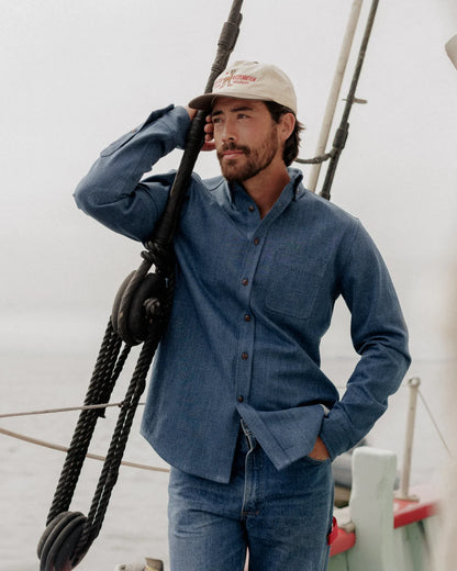 CROPPED PHOTO OF MALE MODEL, LEANING ON SAILBOAT LINE, WEARING DARK BLUE DENIM SHIRT AND JEANS, WHITE CAP, SMILING, DARK SHORT HAIR AND FACIAL HAIR