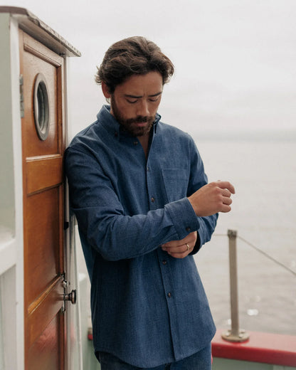 WAIST-UP CROPPED PHOTO OF MALE MODEL WEARING DARK DENIM SHIRT ON SAILBOAT WITH A GREY BACKGROUND